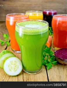 Five tall glasses with the juice of carrot, cucumber, beetroot, tomato and pumpkin with vegetables, parsley on a wooden boards background