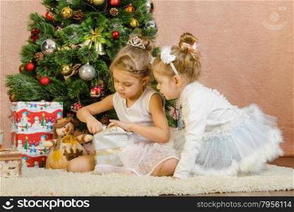 Five-year and three-year girl in a New Year&amp;#39;s dress sitting on a mat at the Christmas tree