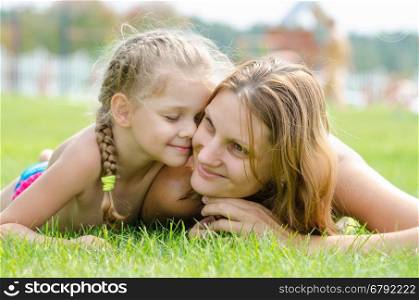 Five-year cute daughter pressed her face to the mother's face on a green grass lawn