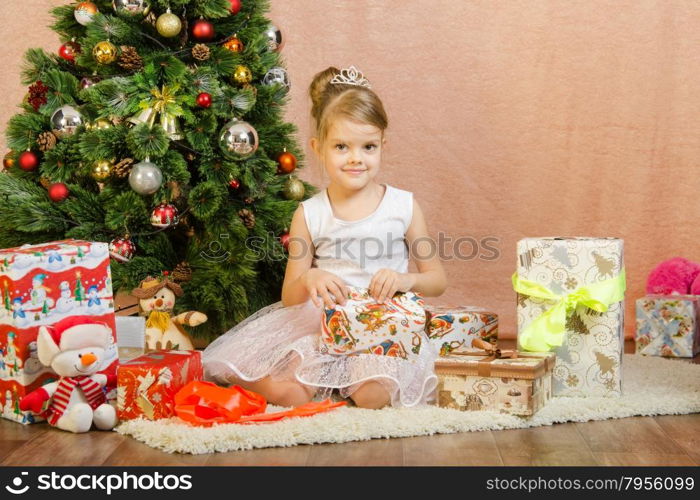 Five-year girl in a New Year&amp;#39;s dress sitting on a mat at the Christmas tree