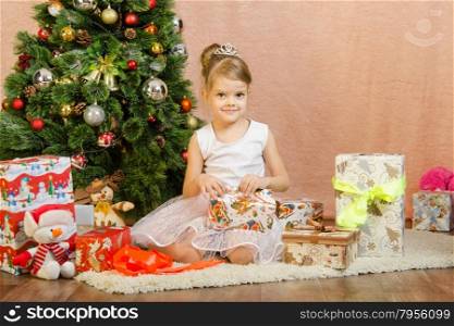 Five-year girl in a New Year&amp;#39;s dress sitting on a mat at the Christmas tree