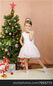 Five-year girl in a New Year&amp;#39;s dress standing on a mat at the Christmas tree