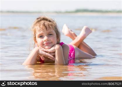 Five-year girl lies in water in the shallows of the river