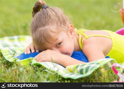 Five-year girl lies on a bed on a green meadow and artfully looks aside
