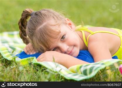 Five-year girl lies on a green meadow and touching looking to the frame
