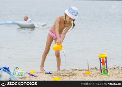 Five-year girl on a beach pouring water from a bucket in the sand. Funny five-year girl playing with sand molds on the beach