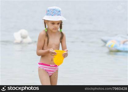 Five-year girl on the beach carrying water in a bucket. Funny five-year girl playing with sand molds on the beach