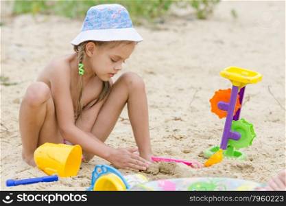 Five-year girl on the river playing in the sand. Funny five-year girl playing with sand molds on the beach