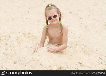Five-year girl with glasses on beach covered with sand up to his waist. Funny five-year girl with glasses on the beach covered with sand up to his waist