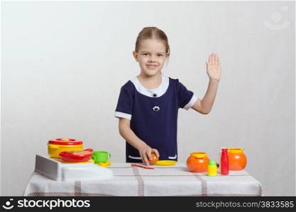 Five year old girl playing in a children&#39;s mistress dishes at a table covered with a cloth
