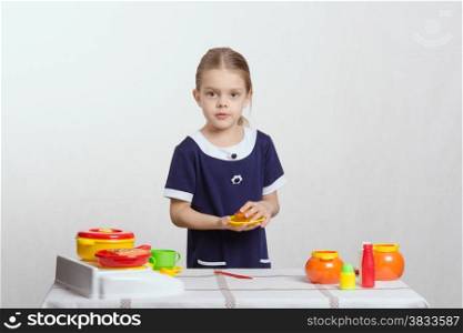Five year old girl playing in a children&#39;s mistress dishes at a table covered with a cloth