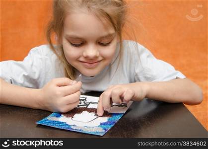 five year old girl sitting at the table and collects sand applique