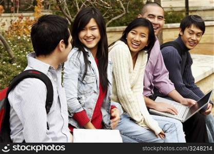 Five young college students sitting together in a college campus and smiling