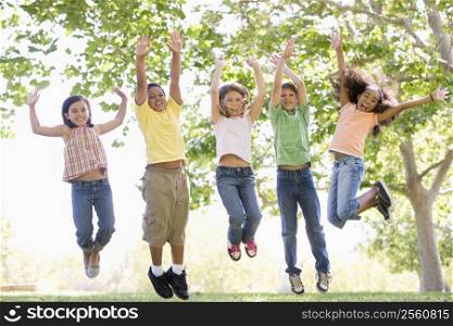 Five young friends jumping outdoors smiling