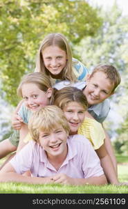 Five young friends piled on each other outdoors smiling