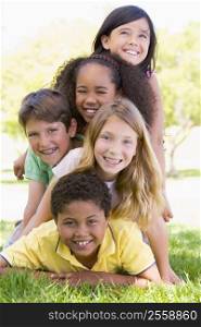 Five young friends piled up on top of each other outdoors smiling