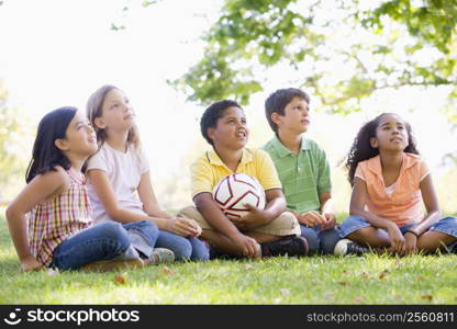 Five young friends sitting outdoors with soccer ball looking up