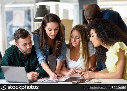 Five young people studying on white desk. Beautiful women and men working together wearing casual clothes. Multi-ethnic group.