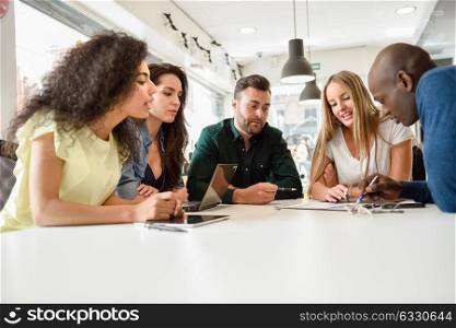 Five young people studying with laptop and tablet computers on white desk. Beautiful girls and guys working toghether wearing casual clothes. Multi-ethnic group smiling.
