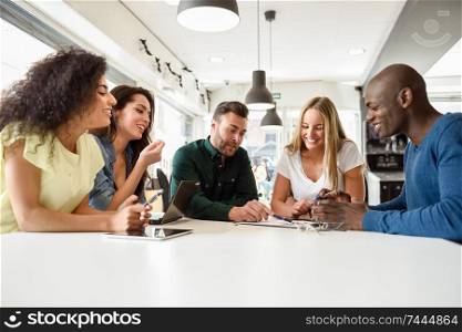 Five young people studying with laptop and tablet computers on white desk. Beautiful girls and guys working toghether wearing casual clothes. Multi-ethnic group smiling.. Multi-ethnic group of young people studying together on white desk
