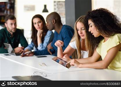 Five young people studying with tablet and laptop computer on white desk. Beautiful women and men working together wearing casual clothes. Multi-ethnic group.