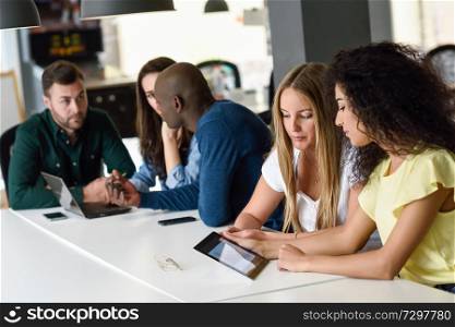 Five young people studying with tablet and laptop computer on white desk. Beautiful women and men working together wearing casual clothes. Multi-ethnic group.. Multi-ethnic group of young people studying with laptop computer