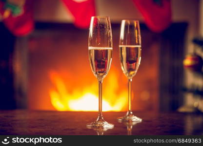 Fizzy champagne in two glasses on Christmas table in front of fireplace