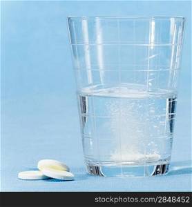 Fizzy vitamin capsule throw in water glass on blue background