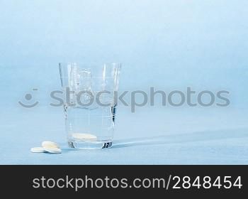 Fizzy vitamin capsule throw in water glass on blue background