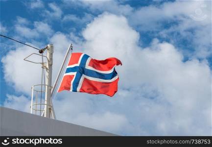Flag of norway flying from the mast of a cruise ship against a blue sunny sky. Norwegian flag flying from mast of cruise ship