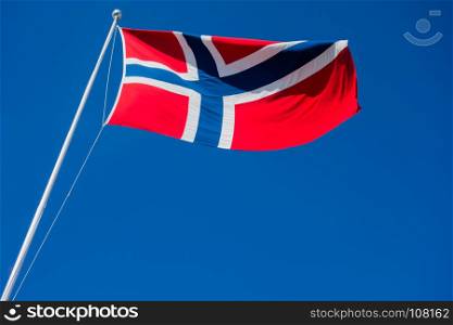 Flag of Norway on pole flapping in wind against clear blue sky.
