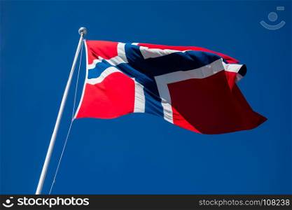 Flag of Norway on pole flapping in wind against clear blue sky.