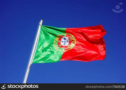 Flag of Portugal flapping in wind against empty blue sky.