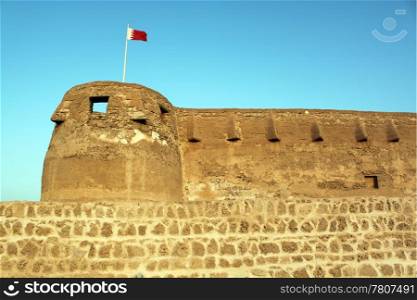 Flag, tower, wall of fort Arad in Manama city, Bahrein