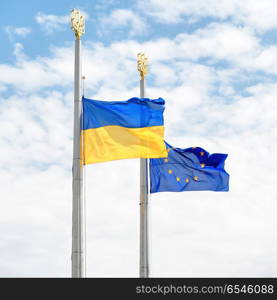 Flags of Europe and Ukraine on the poles with blue sky as background. Flags of Europe and Ukraine