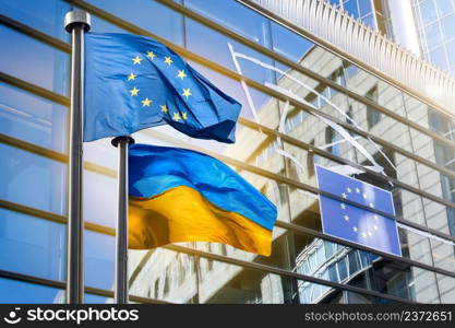 Flags of European Union and Ukraine against European Parliament bulding with logo of EU in Brussels, Belgium