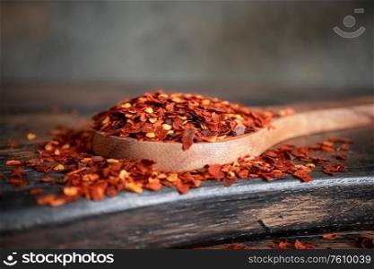 Flakes of red hot chili pepper in wooden spoon closeup on a kitchen table.