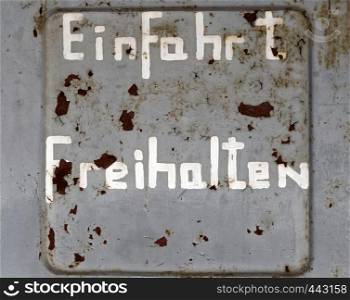 "Flaking old weathered German inscription "Keep entrance free", on an ugly grey wall with too little paint and spots of rust, concept"