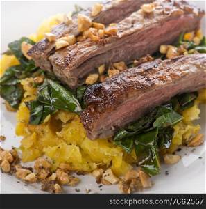 flank steak with mashed plantain , collard greens and ginger peanuts, close up