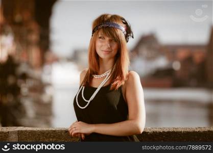 Flapper girl portrait. Retro style fashion vintage woman from roaring 1920s in headband with string of pearls, outdoor. City background