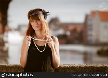 Flapper girl portrait. Retro style fashion vintage woman from roaring 1920s in headband with string of pearls, outdoor. City background