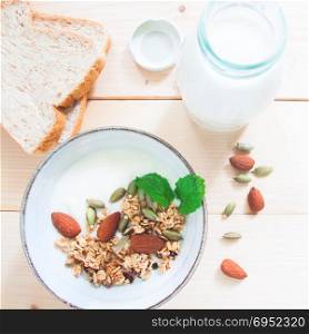 Flat lay bowl of homemade granola with yogurt almond, Whole wheat breads and fresh milk in bottle. Healthy lifestyle concept