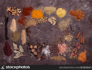 Flat lay composition frame of various spices over brown slate background, top view. Flat lay spicy frame
