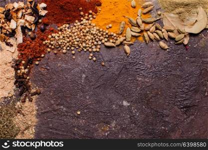 Flat lay composition frame of various spices over brown slate background, top view. Flat lay spicy frame