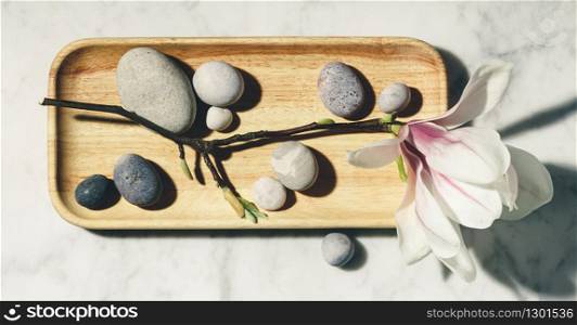 Flat lay composition with beautiful spring magnolia flowers and grey stones on white marble background.