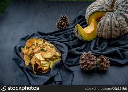 Flat Lay composition with delicious of Homemade crispy pumpkin chips on Black stone texture. Oblique view from the top.