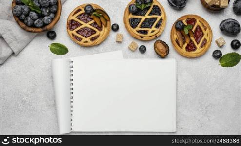 flat lay delicious fruit pies with notebook
