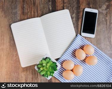 Flat lay design of notebook, smartphone, plant and eggs on wooden table background, spring concept