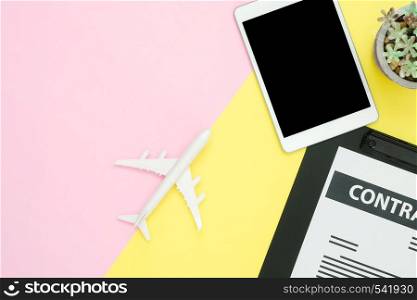 Flat lay design of office desk working space - Top view mock up of contract, plane and black screen tablet with tree on pink yellow pastel color with copy space. Pastel color working space background