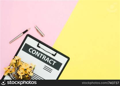 Flat lay design of office desk working space - Top view of a contract document and a pen decorated with yellow flower on pink and yellow pastel color with copy space. Pastel working space background.
